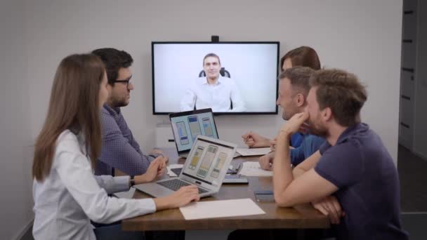 Tým vývojářů mobilních aplikací chatuje videohovory se specialistou v zasedací místnosti v kanceláři — Stock video
