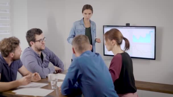 Mujer está realizando en la reunión de negocios en la sala de oficina, sus colegas están sentados en la mesa, escuchando y mirando — Vídeo de stock