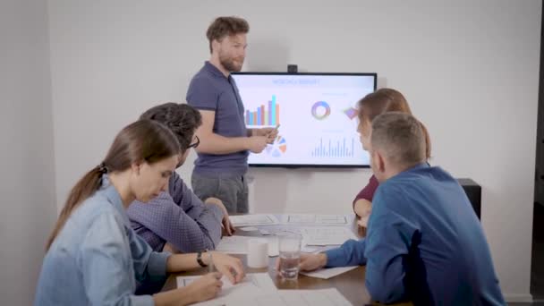 Hombre está presentando informe financiero en la reunión con colegas en la sala de conferencias de la oficina, mostrando gráficos — Vídeo de stock