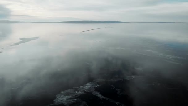 Es una vista aérea. El rápido movimiento de la cámara sobre el río recién congelado. El hielo es liso, con grietas y aire. Las nubes se reflejan en la superficie . — Vídeo de stock