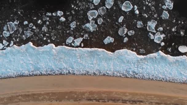 Vista aérea superior desde arriba. Una hermosa vista de diseño de las orillas del río helado. La playa de arena descansa en el borde del hielo, luego los témpanos de hielo individuales flotan en agua fría . — Vídeos de Stock