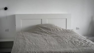 The interior of a modern bedroom. A bright room with white walls, a wide bed with a blanket and a pillow.