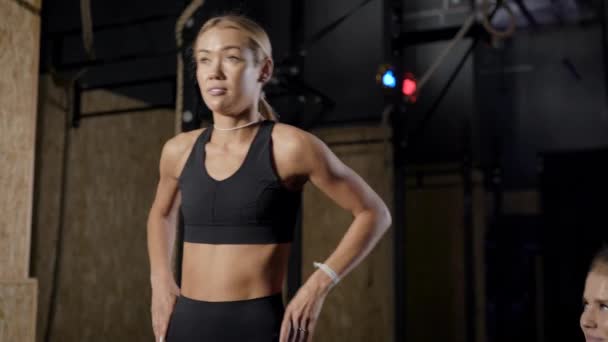 Deux belles jeunes femmes dans la salle de gym. Les filles effectuent des étirements devant l'entraîneur. Blondes fines regarder leur silhouette . — Video