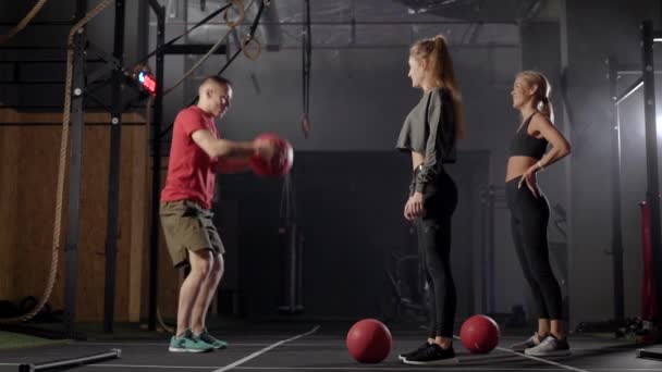 The coachs in the gym. A man shows exercises to two young women. Blondes learn the right technique of exercising. — ストック動画