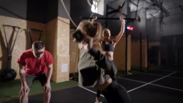 Die Kutschen in der Turnhalle. Ein Mann zeigt zwei jungen Frauen Übungen. Blondinen lernen die richtige Technik des Trainings. — Stockvideo