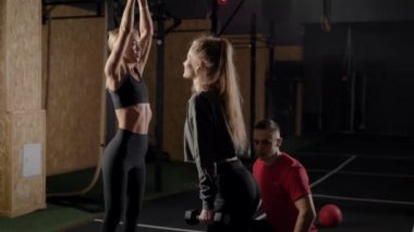 The coachs in the gym. A man shows exercises to two young women. Blondes learn the right technique of exercising.
