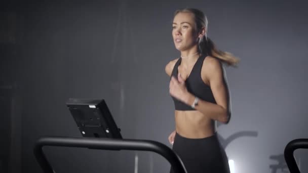 Slender blonde on a treadmill in the gym. A girl with a beautiful figure and a tight-up pres. Running in the gym. — Stok video