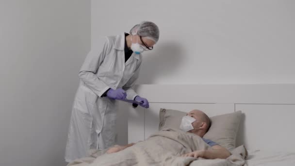 Un hombre enfermo yace en la cama con una alta temperatura. El coronavirus de China afecta los pulmones. Muy cerca hay un médico con guantes protectores. Atepeake. — Vídeos de Stock