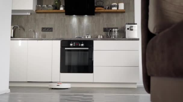 Em uma cozinha moderna elegante é a limpeza. O aspirador de pó robô automático se move ao longo de sua trajetória. Elementos de uma casa inteligente tornam a vida mais fácil para as pessoas — Vídeo de Stock