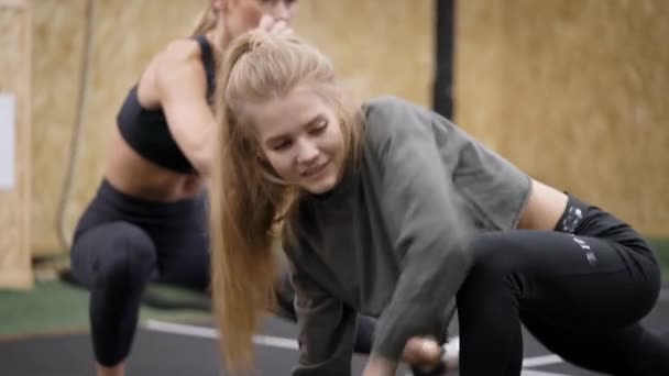 Dos hermosas mujeres jóvenes en el gimnasio. Las chicas realizan estiramientos delante del entrenador. Rubias delgadas observan su figura . — Vídeo de stock