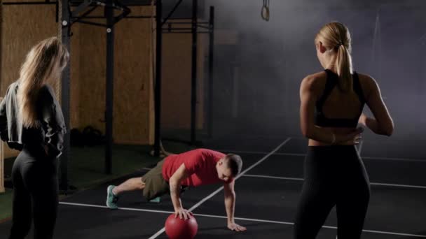 Trenéři v tělocvičně. Muž ukazuje cvičení dvěma mladým ženám. Blondýnky se naučí správnou techniku cvičení.