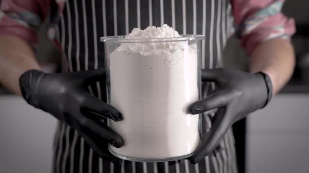 A liszt a tészta fő összetevője. Ismeretlen séf, kezében egy nagy üveg liszttel. Főzés — Stock videók