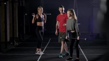 The coachs in the gym. A man shows exercises to two young women. Blondes learn the right technique of exercising.