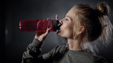 Spor salonundaki genç ve güzel bir kadın. Bir kız koçluk yaparken su içer..