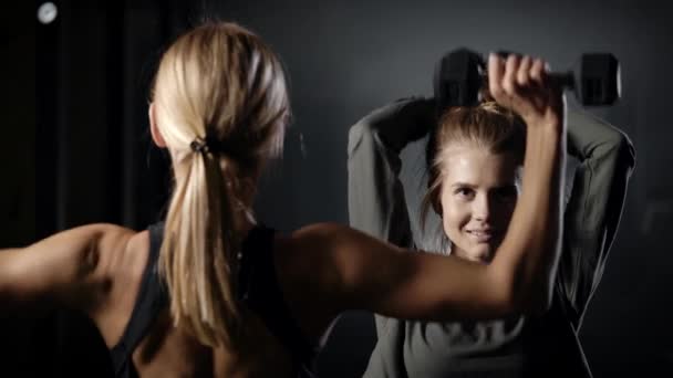 Twee mooie blondjes in de sportschool. Meisjes doen oefeningen met licht gewicht. Het is belangrijk om de gezondheid te controleren en te rekenen. — Stockvideo