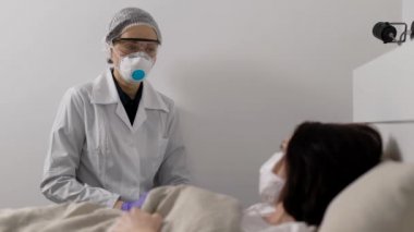 The doctor next to a seriously ill woman. Viral infection is everywhere. The patient is wearing a protective mask. Coronavirus affects the respiratory system.