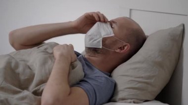 A sick man lies in bed wearing a protective mask. The virus affects the airways. Fever and cough accompany coronavirus. Virus