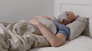 A sick man lies in bed wearing a protective mask. The virus affects the airways. Fever and cough accompany coronavirus. Virus