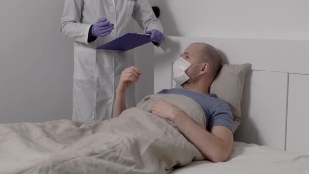 Un hombre enfermo yace en la cama con una alta temperatura. El coronavirus de China afecta los pulmones. Muy cerca hay un médico con guantes protectores. Atepeake. — Vídeos de Stock