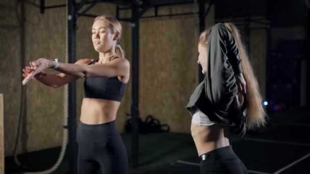 2人の若いスポーツ女性がジムでトレーニングをしたり体の筋肉を温めたりストレッチしたり一緒に陽気におしゃべりしています — ストック動画