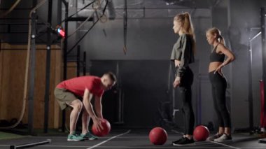 Spor salonundaki spor salonunda koçla antrenman yapan iki sporcu kadın aynı egzersizi tekrarlıyor.