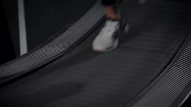 Pies de la deportista se mueven sobre la cinta de correr en el gimnasio, calzados en zapatillas deportivas, vista de detalle — Vídeo de stock