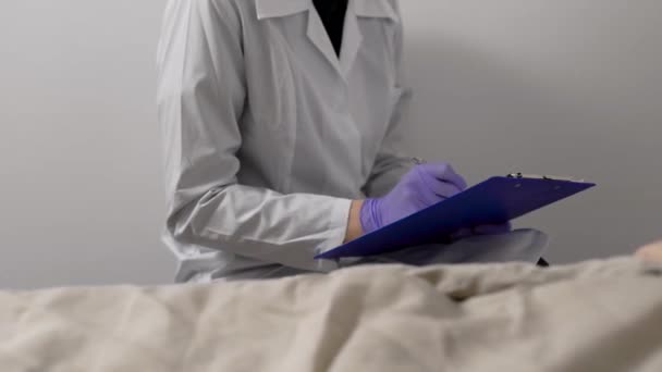 Lekarz wypełnia listę kontrolną i listę wizyt w pokoju szpitalnym pacjenta, siedzącego w pobliżu łóżka — Wideo stockowe