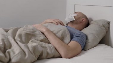 man is suffering by fever, high temperature and cough lying in bed during seasonal epidemic of flu and respiratory infections