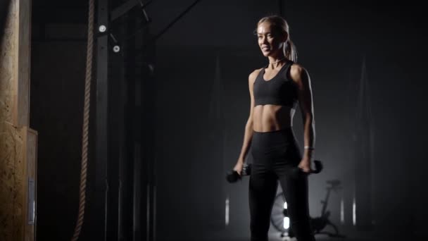 Schlanke Frau macht körperliche Übungen mit Kurzhanteln im Fitnessstudio, kauert mit Gewicht und hält sich fit — Stockvideo