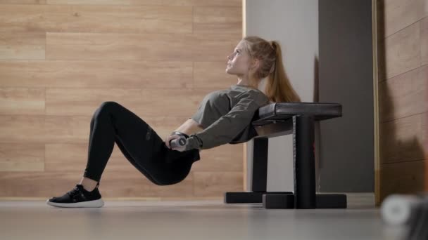 Attractive slim woman is training muscles of ass and legs in fitness hall, leaning on bench by back and moving hips — Stok video