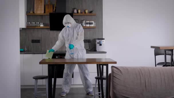 Salgın Covid-19. Koruyucu giysili bir adam odayı dezenfekte ediyor. Özel dezenfektan, yüzeylere püskürtülmüş. — Stok video