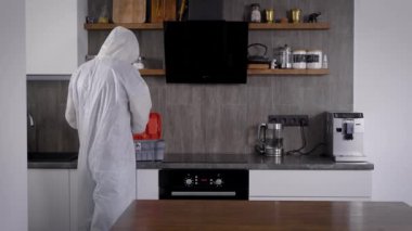 Salgın Covid-19. Koruyucu giysili bir adam odayı dezenfekte ediyor. Özel dezenfektan, yüzeylere püskürtülmüş.