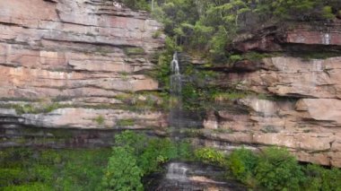 Blue Mountains Ulusal Parkı. Uçurumun ortasındaki şelalede, yeşil ağaçların etrafında.