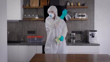 Salgın Covid-19. Koruyucu takım elbiseli, dans eden ve sevinen bir adam. Oda antiseptik ve prosifine ile tedavi ediliyor.