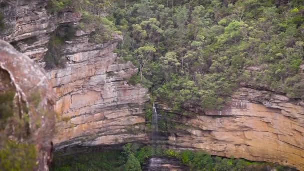 Una hermosa cascada entre las rocas rojas y la vegetación . — Vídeos de Stock