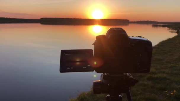 Camera shoots timelapse sunset over the sea on tripod. Review of camera making time laps at the beach on boats shipping in sea, sunset. — Stock Video