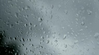 Bulutlu arka planda cam yüzeyine yağmur damlaları düşer. Bulutlu arkaplanda izole edilmiş doğal yağmur damlaları deseni.