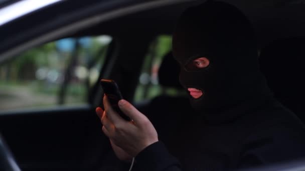 Мужчина в балаклаве, молодой преступник со смартфоном в руках — стоковое видео