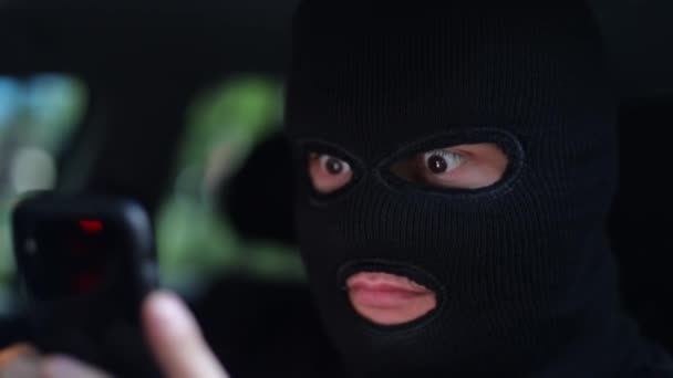 Um homem numa balaclava, um jovem criminoso com um smartphone nas mãos — Vídeo de Stock