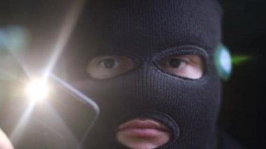 Maskeli bir soyguncu kamera lensine fener tutar.