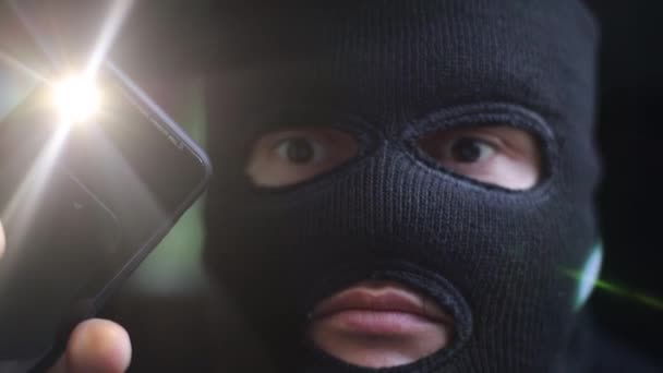 Террорист с фонариком в темной маске смотрит в камеру — стоковое видео