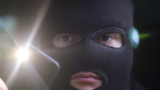 A robber in a mask shines a flashlight into the camera lens — Stock Video