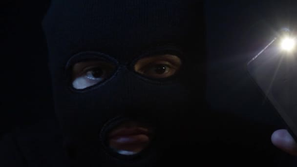 A criminal in a balaclava with a flashlight in his hands — Stock Video