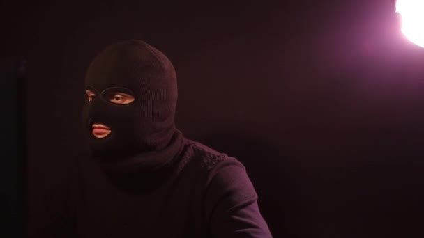 Kar maskeli bir adam karanlık bir odada dizüstü bilgisayarla çalışıyor. — Stok video