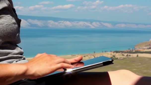 Dziewczyna za pomocą tabletu, zbliżenie, piękny widok na jezioro Bajkał, krajobraz — Wideo stockowe