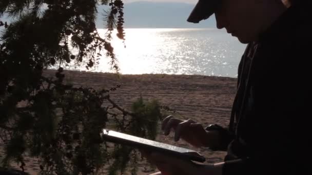 Flicka använder en surfplatta på Baikal stranden — Stockvideo