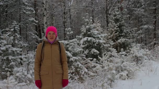 눈 동안 눈 덮인 겨울 숲에서 밝은 분홍색 모자에 있는 여자의 초상화 — 비디오