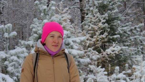 눈 동안 눈 덮인 겨울 숲에서 밝은 분홍색 모자에 있는 여자의 초상화 — 비디오