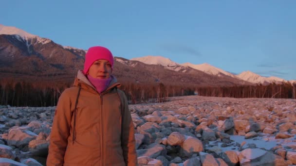 Retrato de una joven sonriente al pie de las montañas al atardecer — Vídeos de Stock