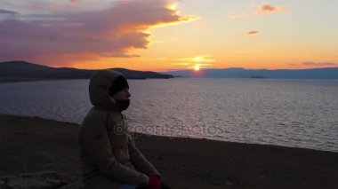 Kız deniz kıyısında oturur ve mesafe içine görünüyor. Güzel gün batımı